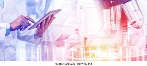 Science Lab Research And Development Concept - Scientist Holding Tablet Computer With Scientific Instrument, Microscope And Chemical Test Tube In Laboratory Background.