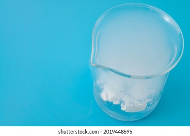 Science Laboratory, Scientific Experiment And Lab Test Concept With Dry Ice In A Glass Chemistry Beaker Isolated On Blue Background With Copy Space