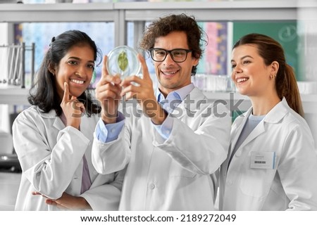 science research, gene technology and people concept - international group of happy smiling scientists with green leaf in petri dish working in laboratory