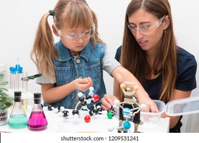 Science School, Workshop. A Woman Teacher And Girl Child Collect Molecules And Conduct Chemical Experiments. On The Table Is A Robot. STEM Education.