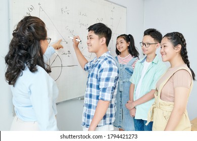 Science teacher explaining theorem to group of students and asking schoolboy to writing equation on whiteboard - Powered by Shutterstock