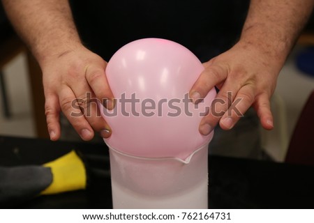 A science teacher puts an inflated balloon into a beaker of liquid nitrogen to show how it collapses and freezes.