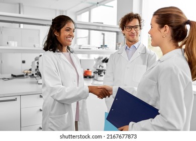 Science, Work And People Concept - International Group Of Happy Scientists Shaking Hands In Laboratory