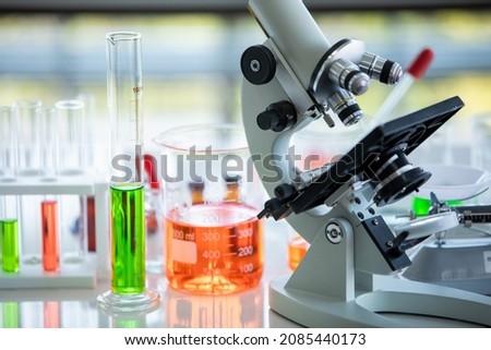 Scientific microscope equipment and chemical liquid solution as biology specimen in glass tube and beaker for pharmaceutical test and medical experiment in chemistry laboratory for health research.