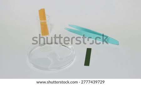 A scientific setup for pH testing featuring litmus paper strips, a petri dish, and tweezers.