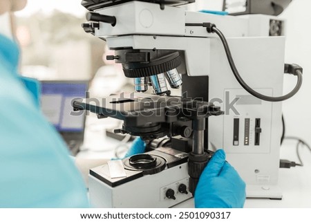 Scientist adjusting microscope, conducting research in a modern laboratory. The lab is equipped with advanced technology, reflecting the cutting edge nature of her work