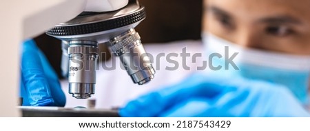 Scientist analyzing microscope slide at laboratory. Young woman technician is examining a histological sample, a biopsy in the laboratory of cancer research