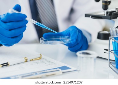 Scientist analyzing samples with pipette in laboratory. Scientist wearing blue gloves is holding a pipette with blue liquid over a petri dish, conducting research in a laboratory setting. - Powered by Shutterstock