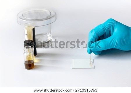 A scientist applies sample solution onto a Thin Layer Chromatography (TLC) plate using a capillary tube for laboratory analysis and separation.