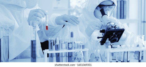 scientist in biohazard protection clothing analyzing covid 19 sample with microscope and holding coronavirus covid 19 blood sample tube on hand in laboratory, coronavirus covid 19 vaccine research