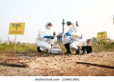 Scientist Or Biologist In A Protective Suit And Mask, Collects Sample Of Waste Water From Industrial