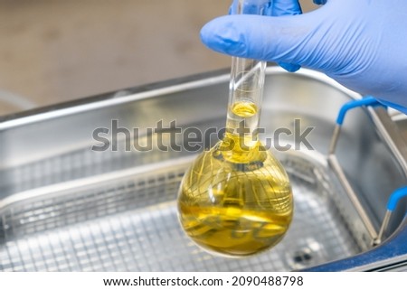 Scientist in blue rubber puts a yellow solution in the flask for dissolving or extraction into ultrasound bath. Urea analysis. Clinical, toxicological and forensic analysis. 