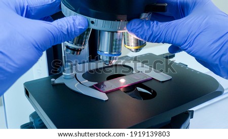 The scientist changes the magnification with two hands
on the microscope, the close up. On the microscope stage, a sample is installed on a glass slide.