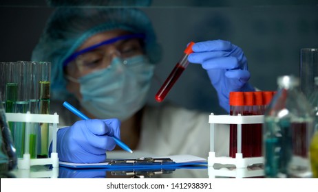 Scientist checking tube with blood analysis and making notes, epidemic outbreak