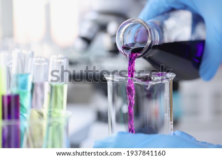 Scientist chemist pouring pink liquid into test tube in lab closeup