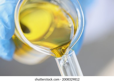 Wissenschaftlicher Chemiker, der gelbes Öl aus dem Glasgefäß in das Reagenzglas gießt, Nahaufnahme
