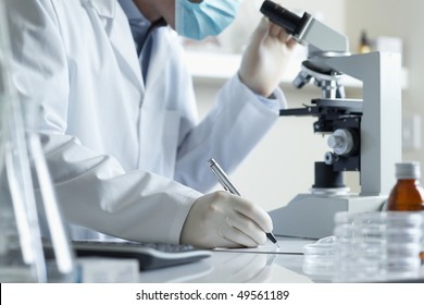 Scientist Conducting Research Taking Notes Whilst Looking Through Microscope Selective Focus