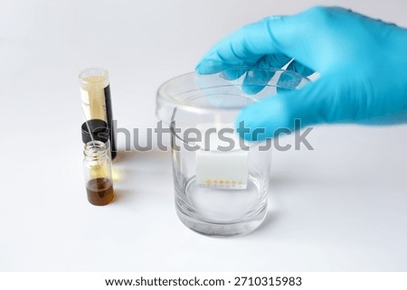 A scientist covers a Thin Layer Chromatography (TLC) developing tank with a glass lid to ensure chamber saturation and start the chemical separation process.
