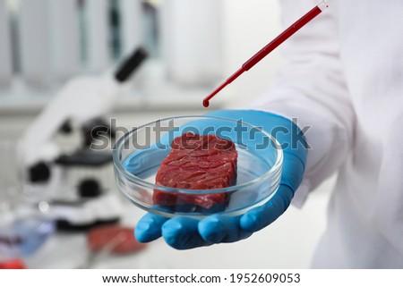Scientist dripping red liquid onto cultured meat in laboratory, closeup