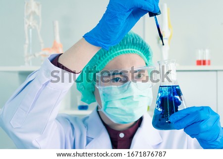 Scientist dropping a blue solution into Science bottle and looking. Chemical liquid for research or analyzing a sample into a bottle in modern laboratory Chemistry. Sensitive focus on Science bottle.
