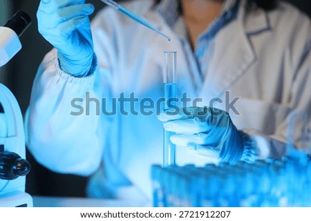 Scientist dropping liquid into test tube using pipette in laboratory, conducting research or experiment in modern laboratory.