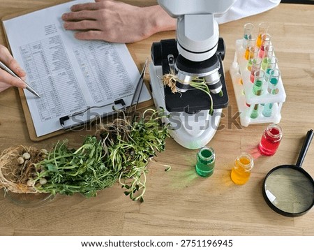 Scientist examines plant samples using a microscope and records data in a laboratory setting with colorful test tubes