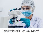 A scientist examines samples with a microscope in a laboratory with test tubes filled with colorful liquids in the background.