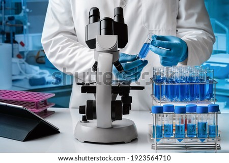 Scientist examining a fluid sample with the microscope in the chemistry lab. Researcher working with samples and microscope in the research laboratory