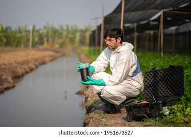 A Scientist In Full Body Protective Suit Measuring The Quality Of Sample Of Water In The The Agricultural Farm.