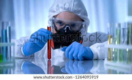 Scientist in gas mask holding test tube with dangerous substance, biohazard