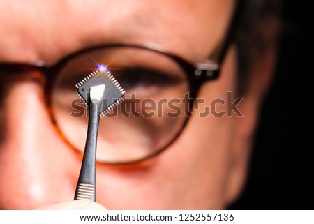 A scientist with glasses is looking at a microchip. The concept of science and artificial intelligence.