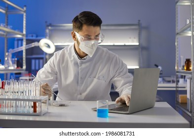 Scientist In Glasses And Mask Doing Research In Science Laboratory. Lab Worker, Assistant Or Medical University Student In Goggles Entering Data Analysis Report In Electronic System On Laptop Computer