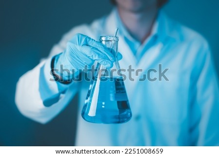 Scientist hand hold erlenmeyer flask with stirring rod filled with blue sample chemicals in chemistry science laboratory. Glassware in medical research. Scientific lab for Biotechnology.