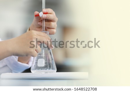 Scientist is holding burette and erlenmeyer flask. free space on right. Focus on finger holding burette.