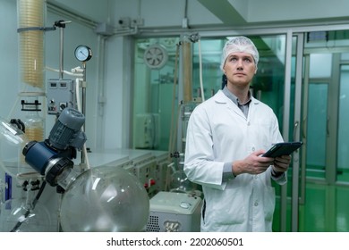 Scientist Holding Paper Board And Checking Rotational Vaporizer During CBD Oil Extraction, Hemp Oil Extraction Process.