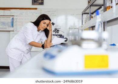 A scientist in a lab analyzes data while using a microscope, surrounded by various lab equipment and scientific materials on a white tabletop.