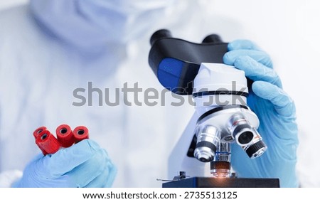 Scientist in lab coat examining samples through microscope with test tubes, sunlight.