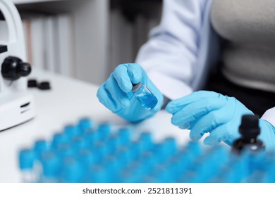 Scientist in Laboratory Handling Blue Liquid Samples with Microscope and Test Tubes - Powered by Shutterstock