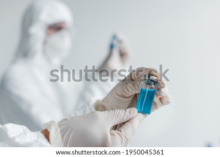 Scientist in latex gloves holding vaccine near colleague on blurred background