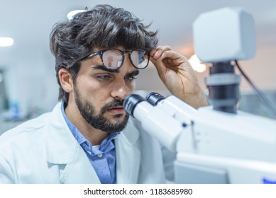 Scientist looking through a microscope. scientist researching. Young laboratory scientist looking at microscope in lab. Scientist looking through microscope while working on research in a laboratory 