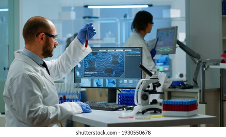 Scientist Man Examining Blood Samples And Liquid Working In Modern Equipped Laboratory. Team Of Doctors Analysing Vaccine Evolution Using High Tech Researching Diagnosis Against Covid19