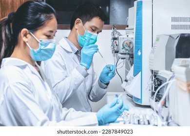 Scientist man injects sample with micro syringe into Mass Spectrometer to analyze samples, scientist woman assisted preparing samples for analysis. Mass spectrometry is used to measure mass per charge
