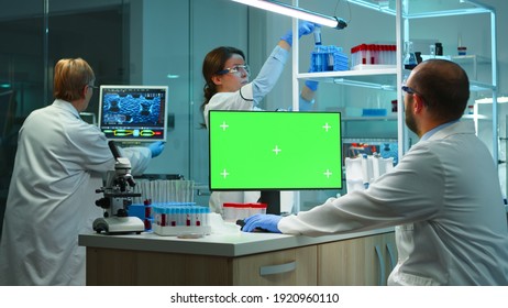 Scientist Man Typing On Computer With Green Mockup In Modern Equipped Lab Working Late At Night. Team Of Microbiologists Doing Vaccine Research Writing On Device With Chroma Key, Isolated Display.