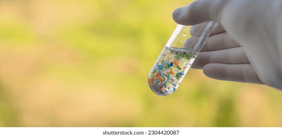 A scientist with medical gloves holding a test tube full of micro plastics collected from the beach. Concept of water pollution and industrial waste management.