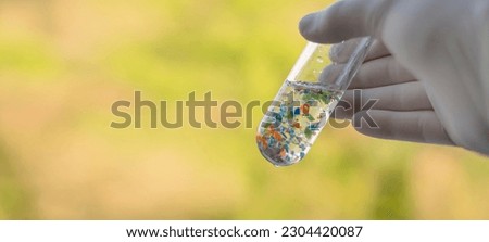 A scientist with medical gloves holding a test tube full of micro plastics collected from the beach. Concept of water pollution and industrial waste management.