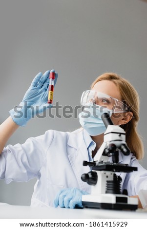 scientist in medical mask and goggles holding test tube with covid lettering in laboratory