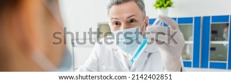 scientist in medical mask holding test tube near blurred colleague, banner