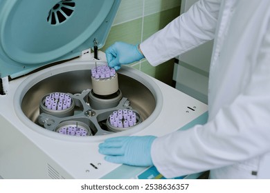 Scientist operating laboratory centrifuge machine, wearing protective gloves and handling test tube rack with care. Centrifuge rotor containing multiple test tubes - Powered by Shutterstock