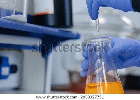 Scientist pipetting orange solution into flask in laboratory.