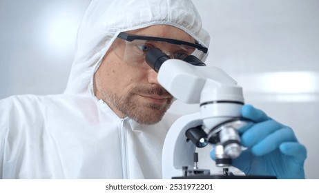 Scientist in ppe analyzing samples with microscope. Close-up of a focused researcher in a lab coat and protective gear using a microscope in a laboratory setting - Powered by Shutterstock